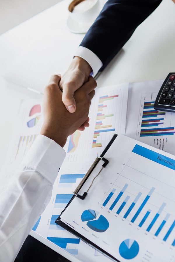 Top view of Business people handshaking over financial graph paper on table
